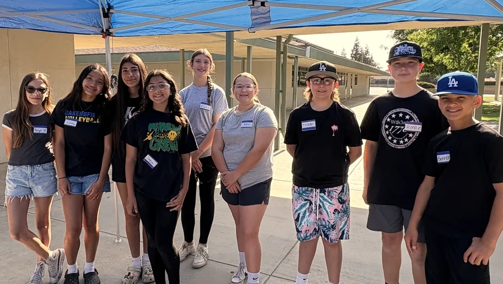 A group of middle school students stands together under a canopy on a school walkway
